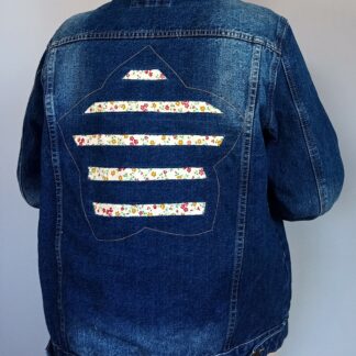 Blouson jean stone avec motif fleur dans le dos. Tissu à fleur apparent dans découpes du motif. Photo porté vue dos.