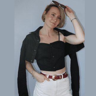 ensemble caraco court + cache-épaule noir porté sur un pantalon blanc. Le ventre apparaît. Vue de trois quart. le cache épaule est posé sur les épaules du modèle. Les manches tombent sur les côtés.