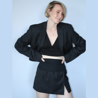 Ensemble veste et jupe réalisé à partir d'une veste d'homme coupée. Veste courte manches longues col tailleur, épaules larges, taille cintrée . Jupe courte, fendue, large bande de bord côte à la taille. Photo porté sur un haut court noir. Vue face.